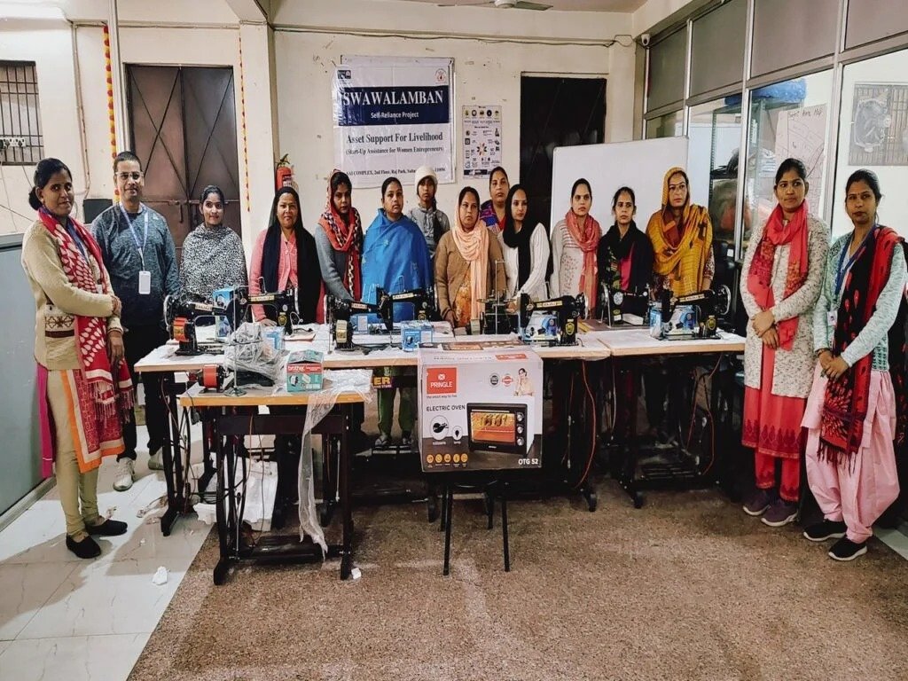 Women standing with sewing machines and livelihood equipment after a CWS asset-support program
